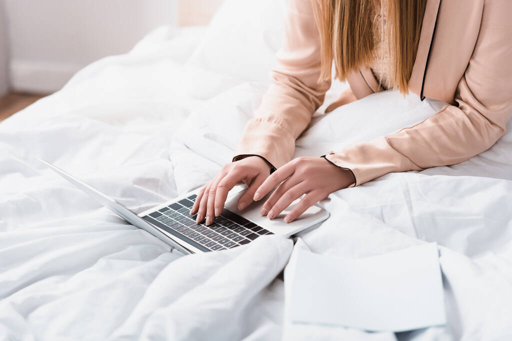 vista parziale di giovane freelance in accappatoio di seta utilizzando il computer portatile in camera da letto - Foto, immagini