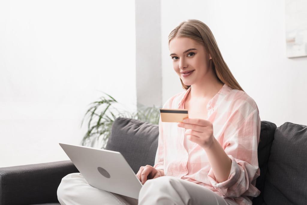 young smiling woman holding credit card near laptop while e-shopping at home - Photo, Image