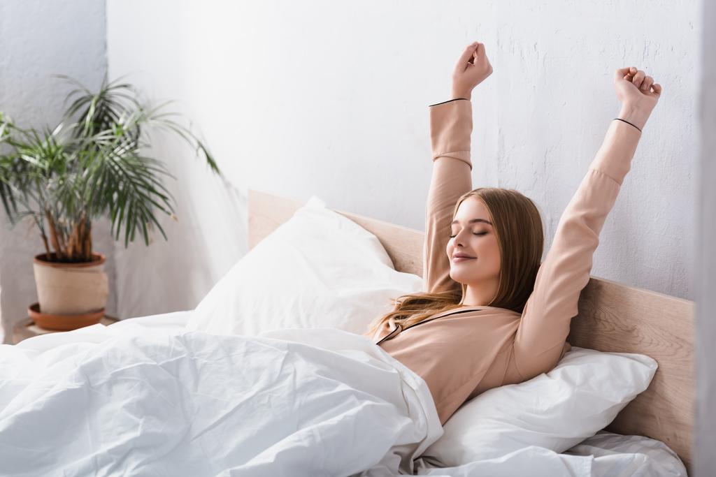wach und fröhlich Frau in Satin Pyjama Stretching im Bett - Foto, Bild