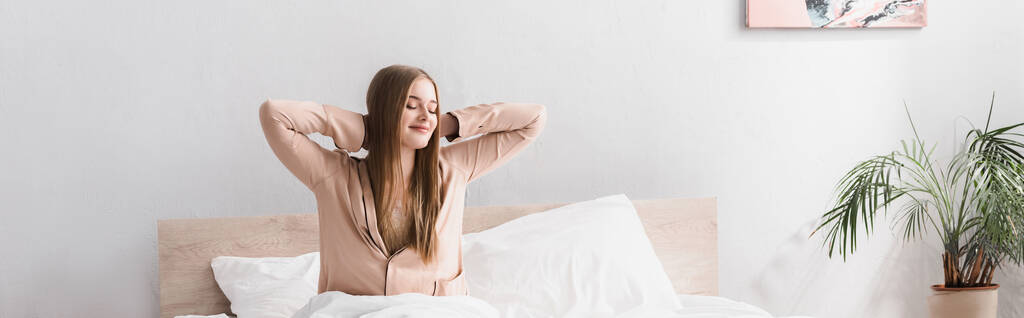 wakker en vrolijk vrouw in satijnen pyjama stretching in bed, banner - Foto, afbeelding