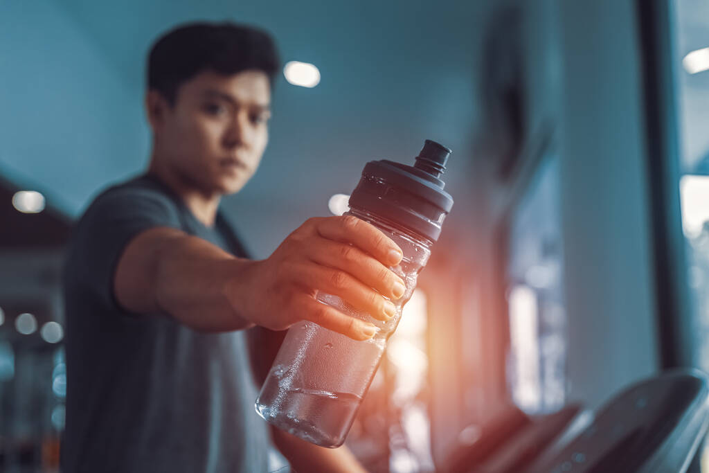 A man in running on treadmill at gym and holding bottle of water - Photo, Image