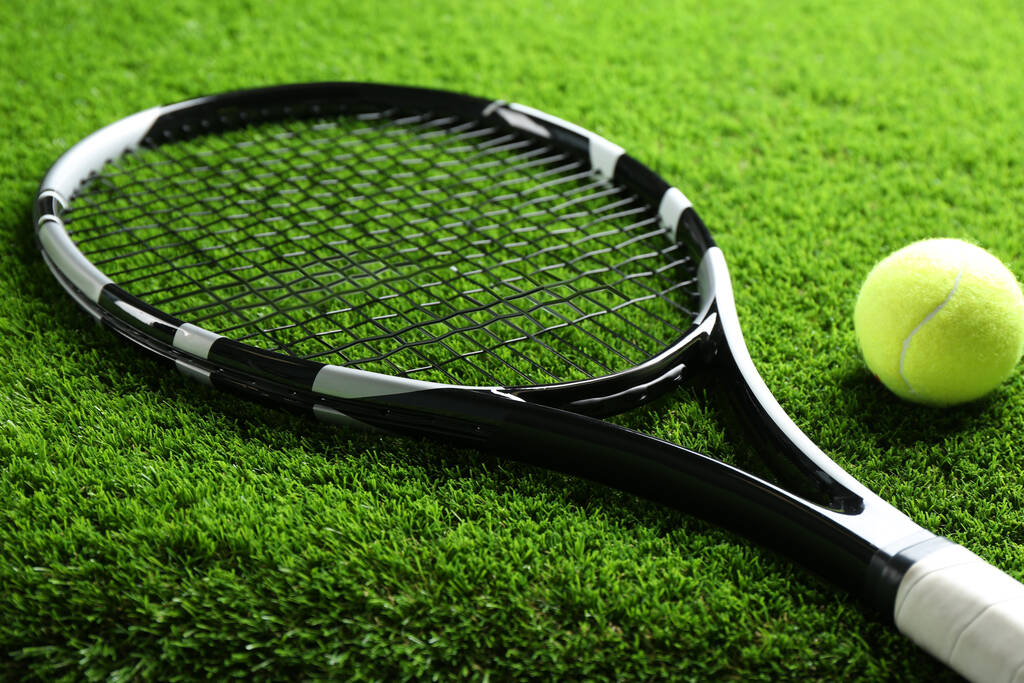 Ρακέτα του τένις και μπάλα στο πράσινο γρασίδι, κοντινό πλάνο. Αθλητικός εξοπλισμός - Φωτογραφία, εικόνα