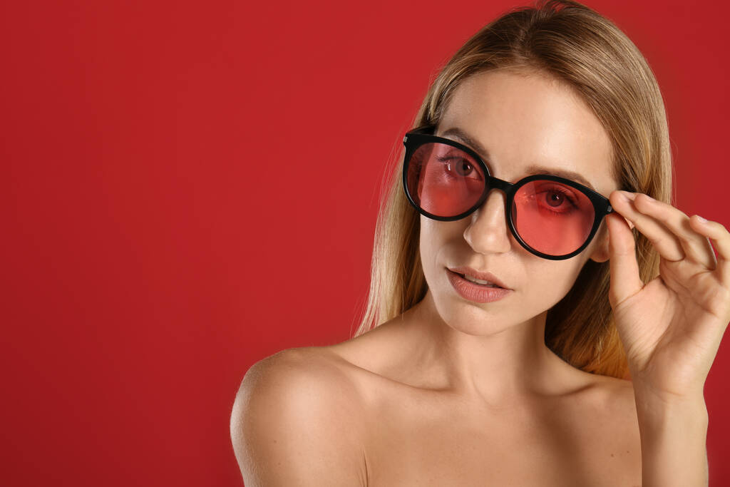 Mooie vrouw met een stijlvolle zonnebril op rode achtergrond. Ruimte voor tekst - Foto, afbeelding