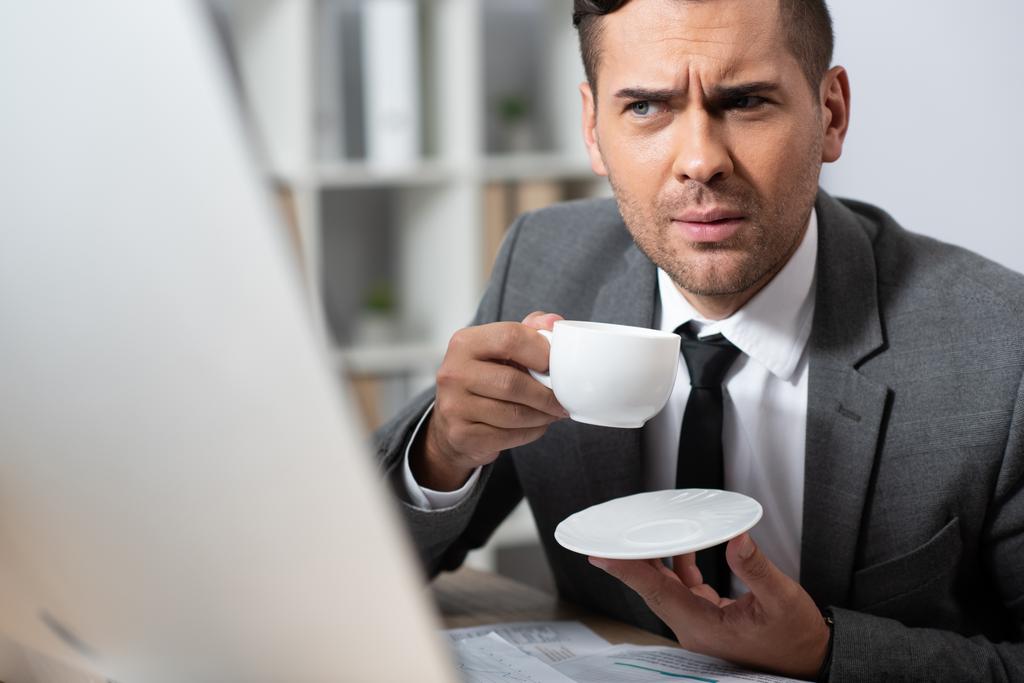 nachdenklicher Geschäftsmann mit Kaffeetasse am Arbeitsplatz, verschwommener Vordergrund - Foto, Bild