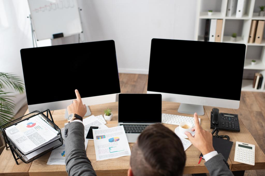 widok ogólny przedsiębiorcy wskazującego palcami na monitory z czystym ekranem  - Zdjęcie, obraz