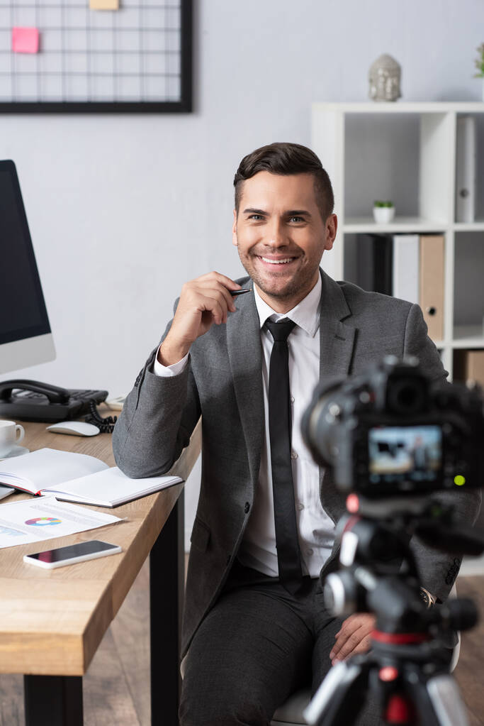 улыбающийся бизнесмен записывает видео на цифровую камеру, размытый передний план - Фото, изображение