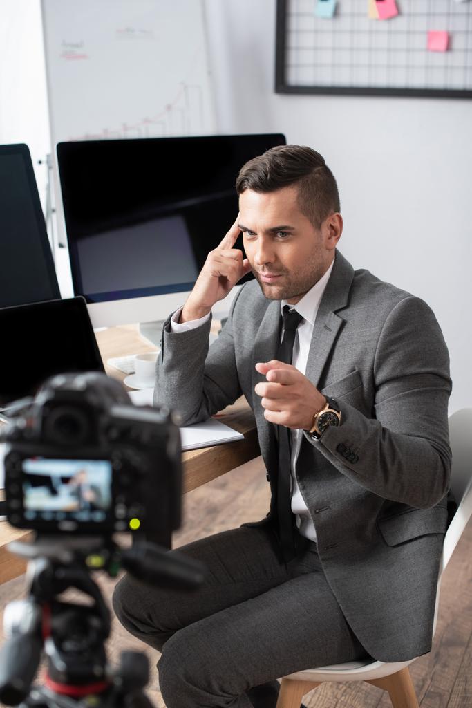 commerciante seduto vicino ai monitor del computer e che punta con il dito alla fotocamera digitale  - Foto, immagini