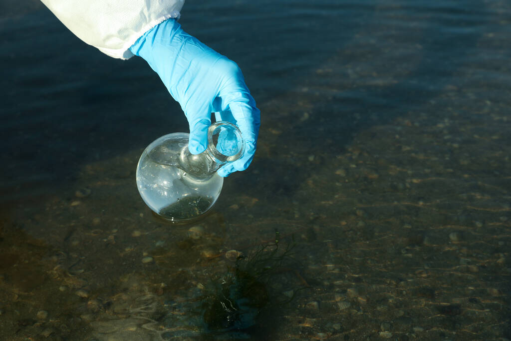 Naukowiec z kolbą florencką pobierający próbkę z rzeki do analizy, zbliżenie - Zdjęcie, obraz