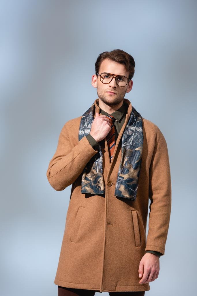 Трогательный мужчина в очках и зимнем пальто стоит на сером - Фото, изображение
