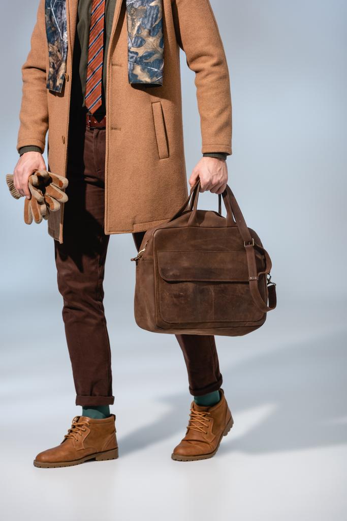 обрезанный вид стильного человека в зимнем пальто с кожаным портфелем и перчатками на сером  - Фото, изображение