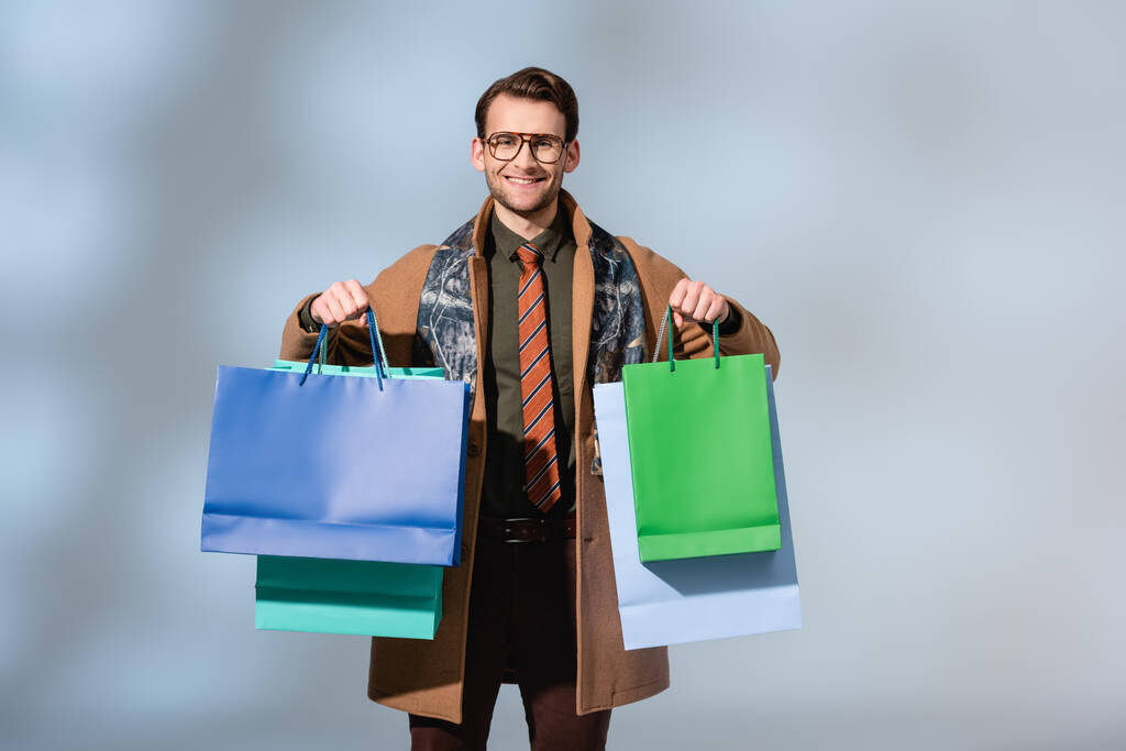 pozitivní zákazník v brýlích drží papírové tašky na šedé - Fotografie, Obrázek