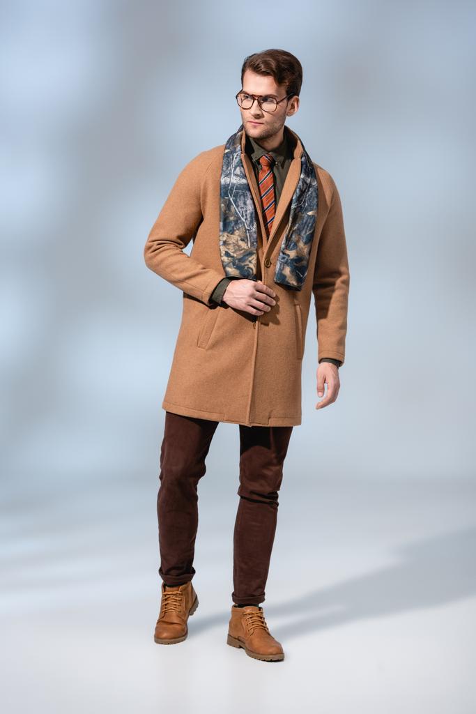 volledige lengte van trendy man in winterjas en bril staand op grijs - Foto, afbeelding