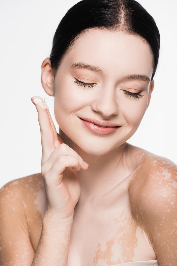 sorridente giovane bella donna con vitiligine applicando crema cosmetica isolata su bianco - Foto, immagini