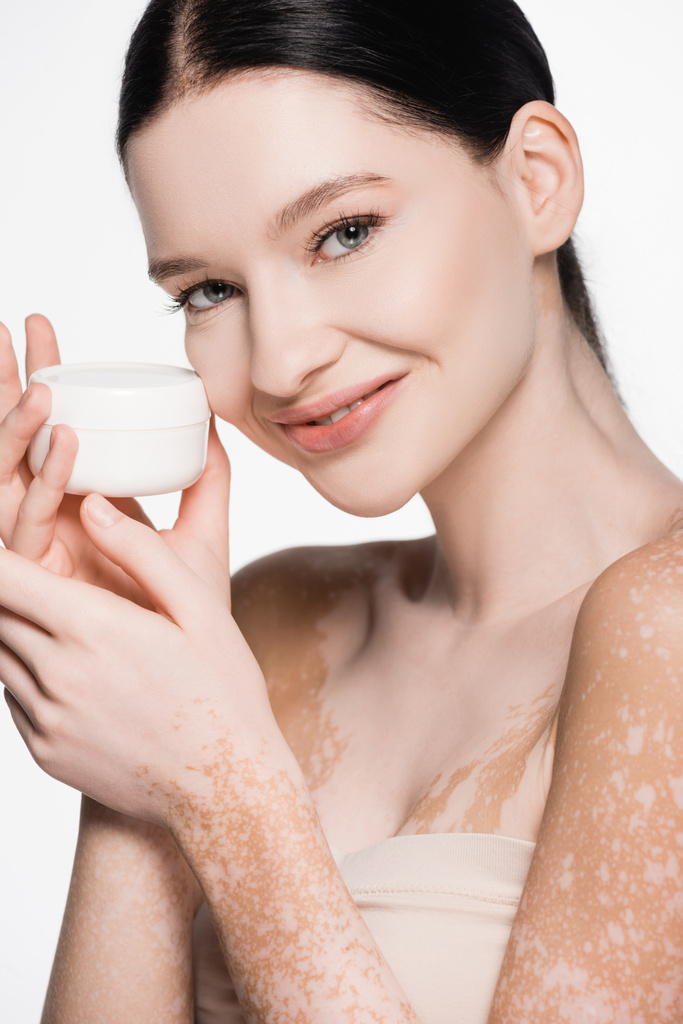 sorridente giovane bella donna con vitiligine tenuta crema cosmetica isolata su bianco - Foto, immagini