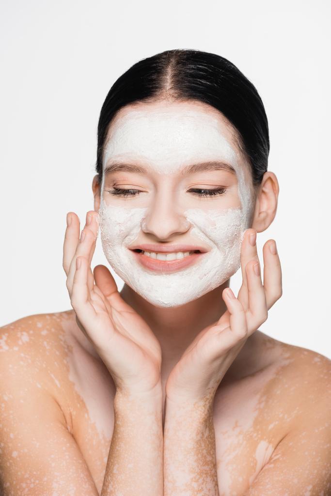 sonriente joven hermosa mujer con vitiligo y máscara de arcilla en la cara aislada en blanco - Foto, imagen