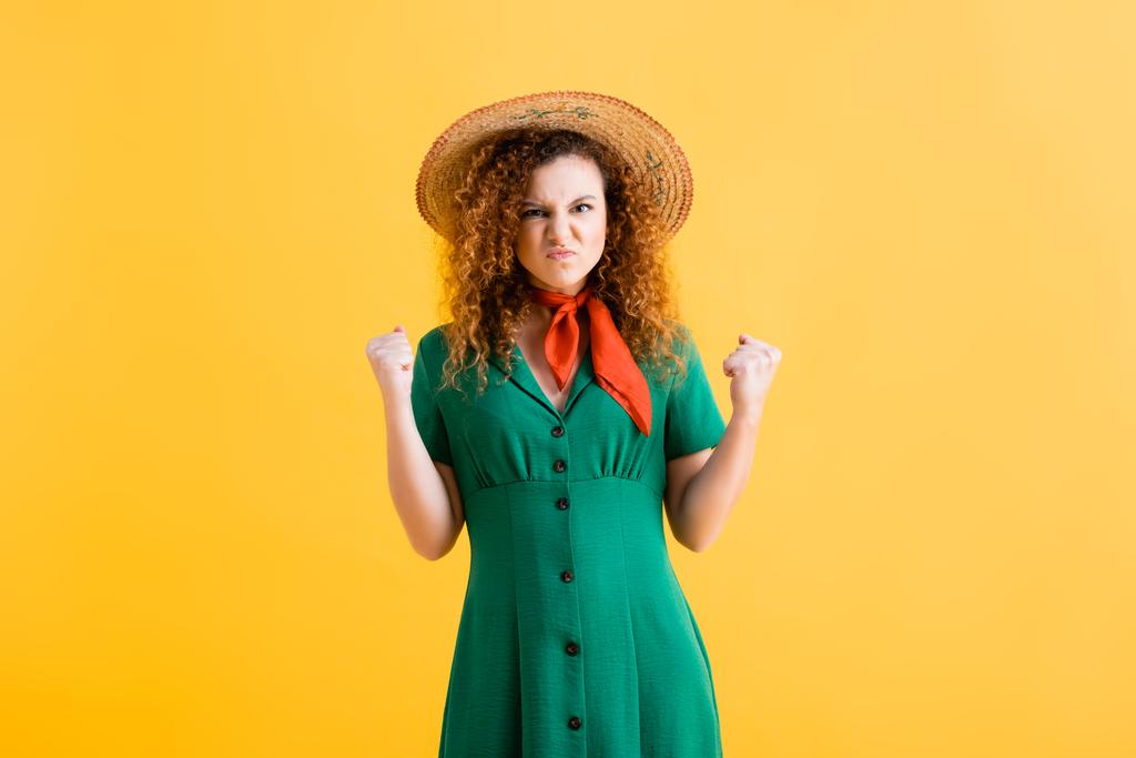 irritated woman in straw hat and green dress standing with clenched fists on yellow  - Photo, Image