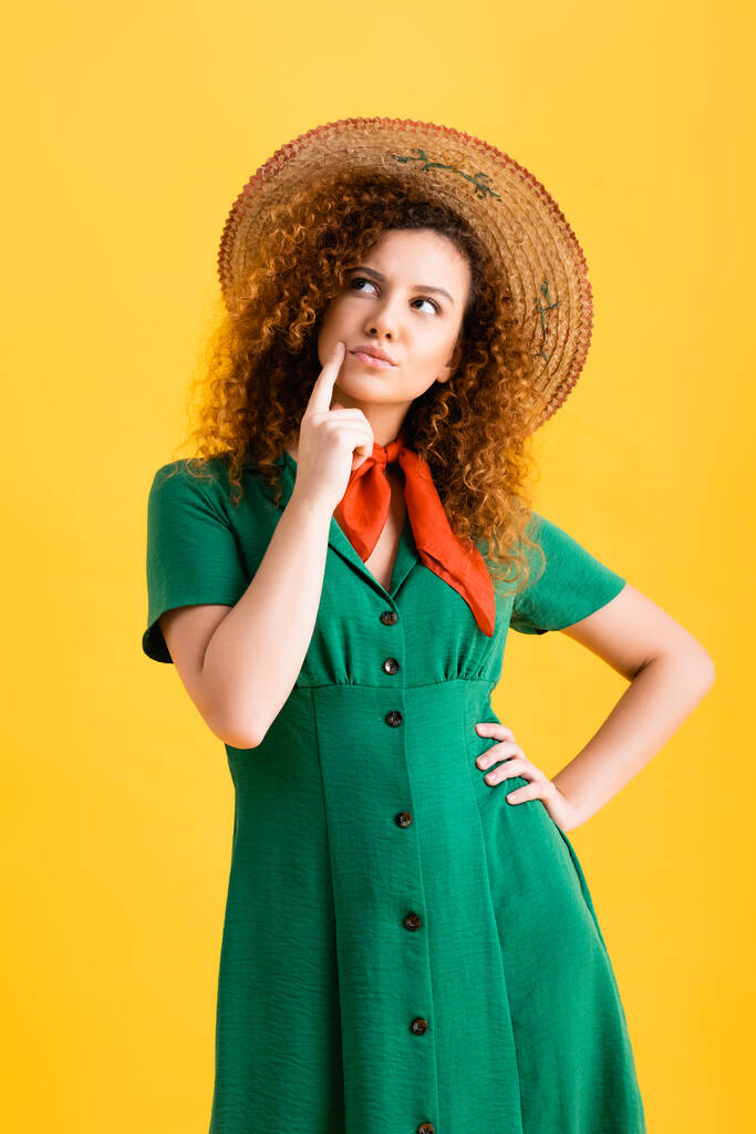 chère jeune femme en chapeau de paille et robe verte debout avec la main sur la hanche sur jaune  - Photo, image