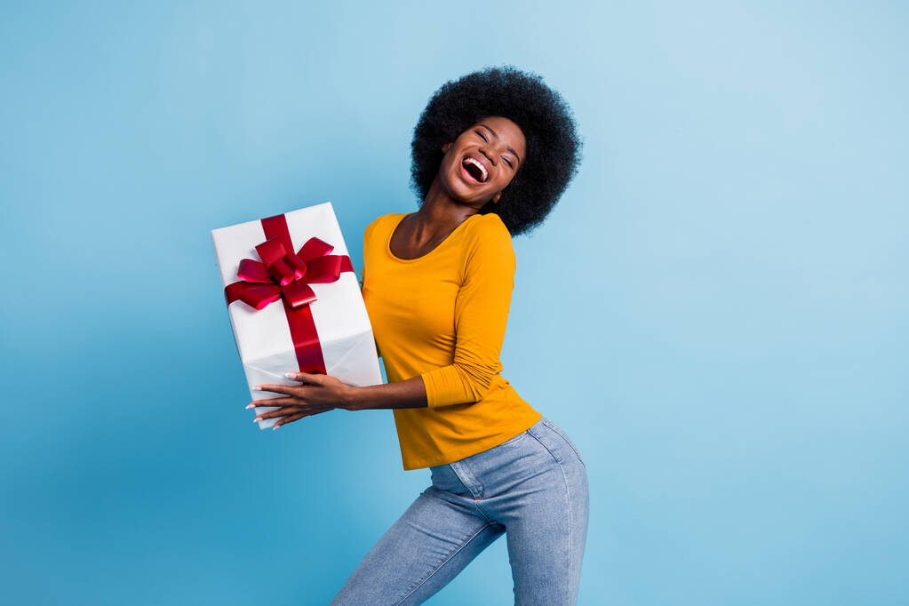 Фотопортрет щасливої усміхненої чорношкірої жінки, що тримає загорнутий подарунок сміється танцює ізольовано на яскраво-блакитному фоні
 - Фото, зображення