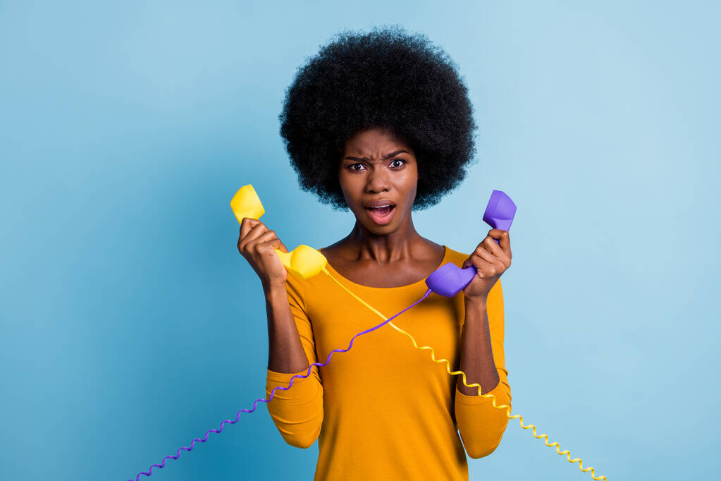 Foto portret van teleurgesteld geïrriteerde gestreste zwarte huid vrouw met retro telefoon handsets geïsoleerd op levendige blauwe kleur achtergrond - Foto, afbeelding