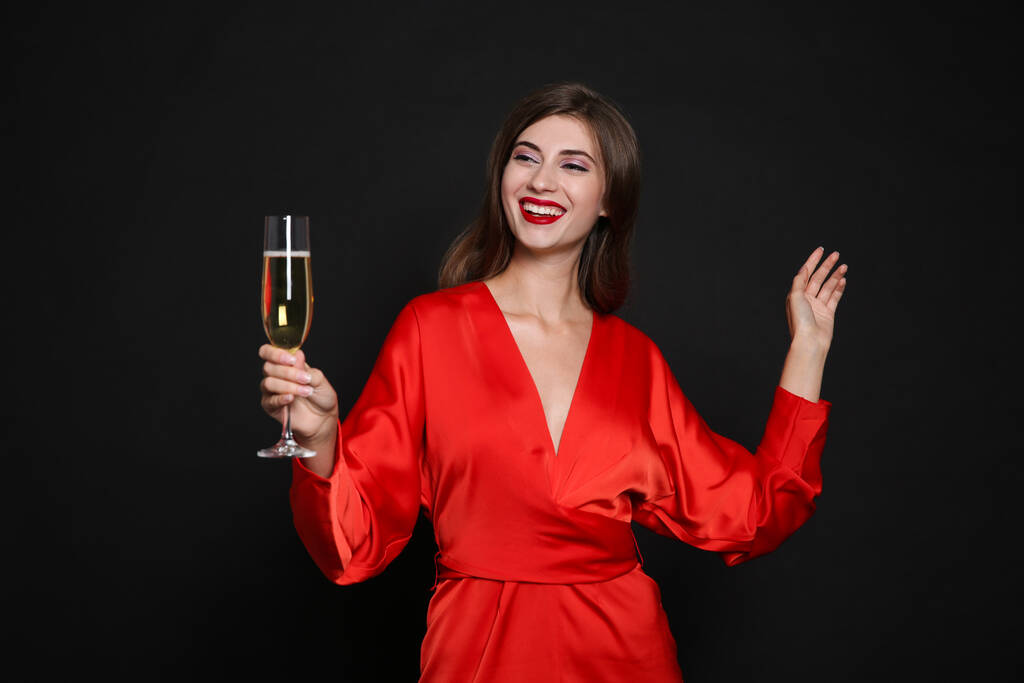 Счастливая женщина с бокалом шампанского на черном фоне. Рождественская вечеринка - Фото, изображение