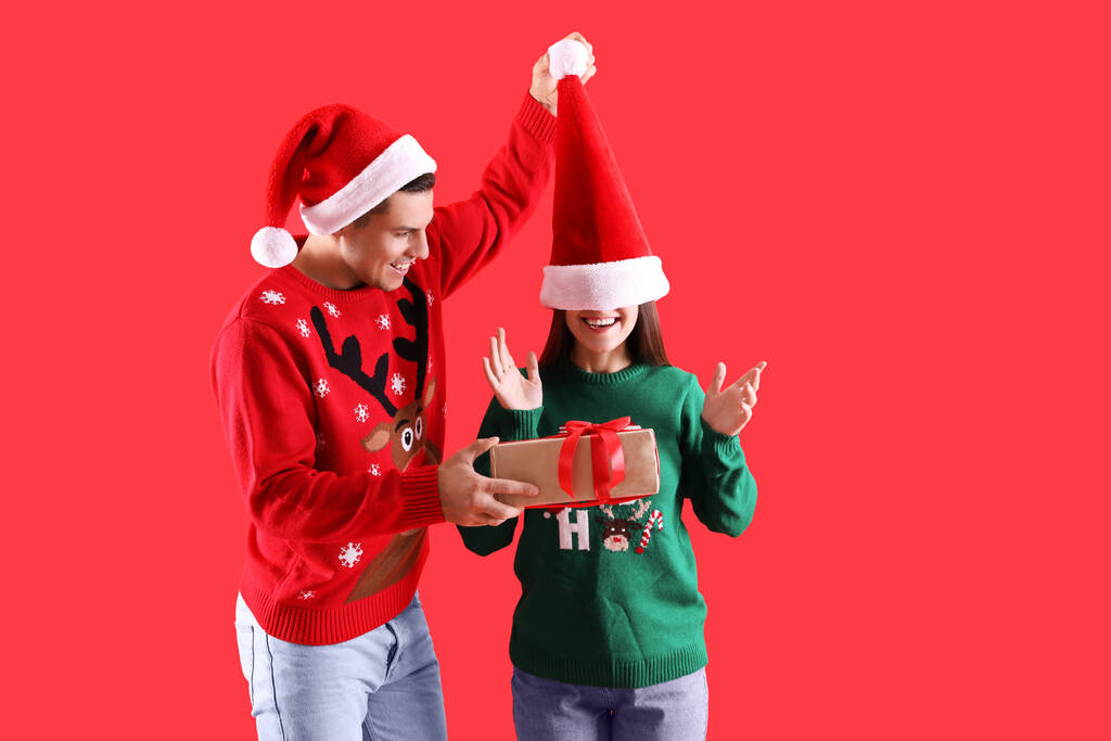 Man presenting Christmas gift to his girlfriend on red background - Photo, Image