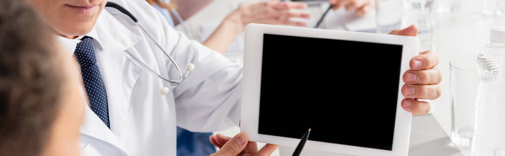 Cropped view of doctor holding digital tablet with blank screen near colleague on blurred foreground, banner  - Photo, Image