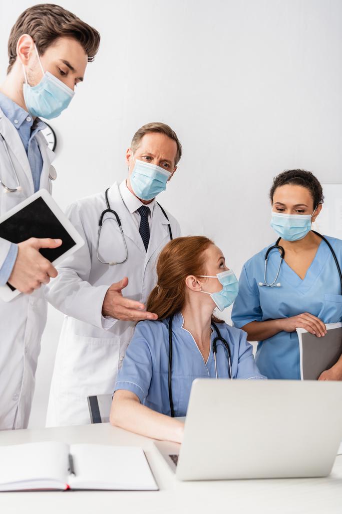Multiculturele verpleegkundigen en artsen die laptop op de werkplek gebruiken op wazige voorgrond - Foto, afbeelding