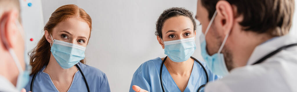 Többnemzetiségű ápolók orvosi maszkban, akik homályos orvosokat figyelnek az előtérben, transzparens - Fotó, kép