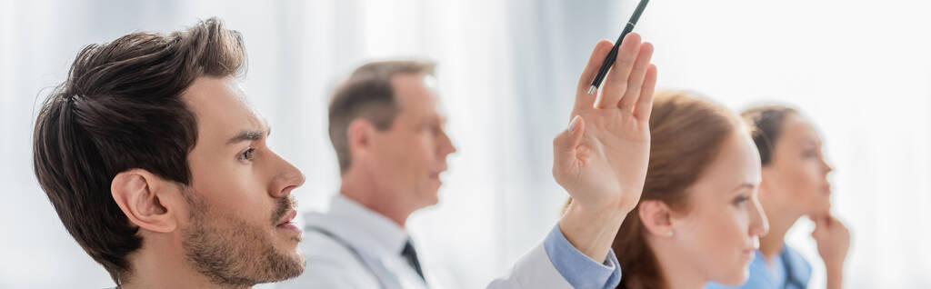 Doctor with raised hand near multicultural colleagues during meeting in hospital on blurred background, banner - Photo, Image