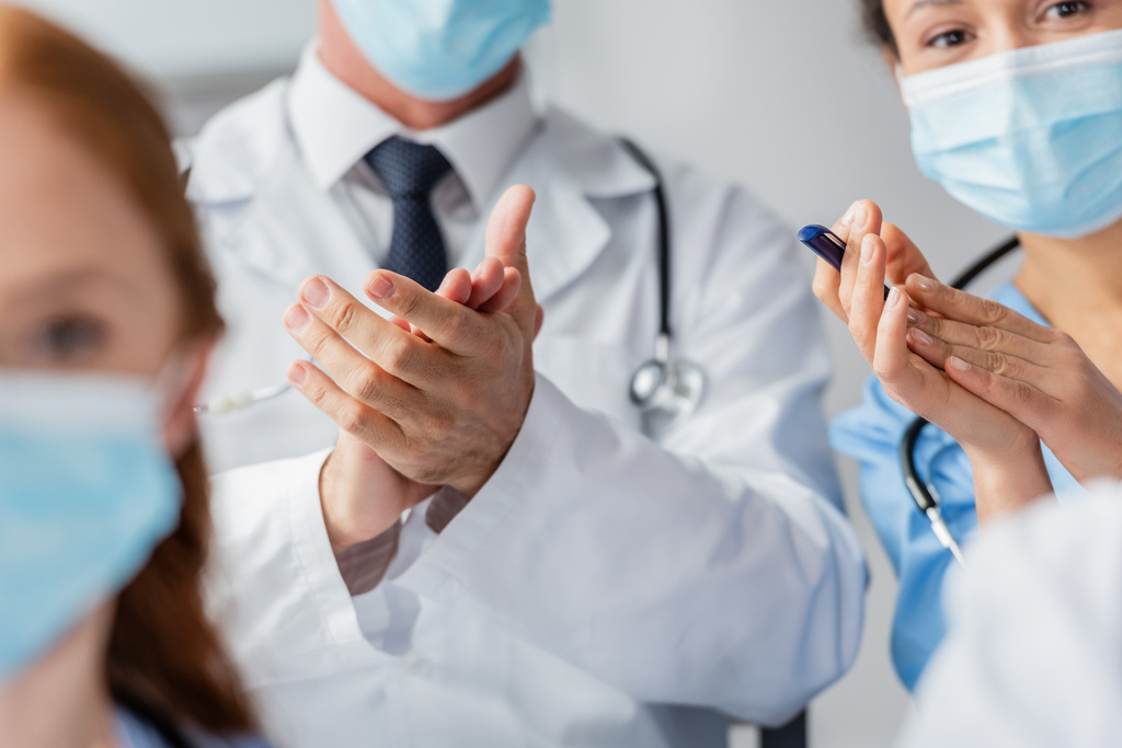 Мультикультурный врач и медсестра аплодируют во время встречи с размытыми коллегами на переднем плане в больнице - Фото, изображение
