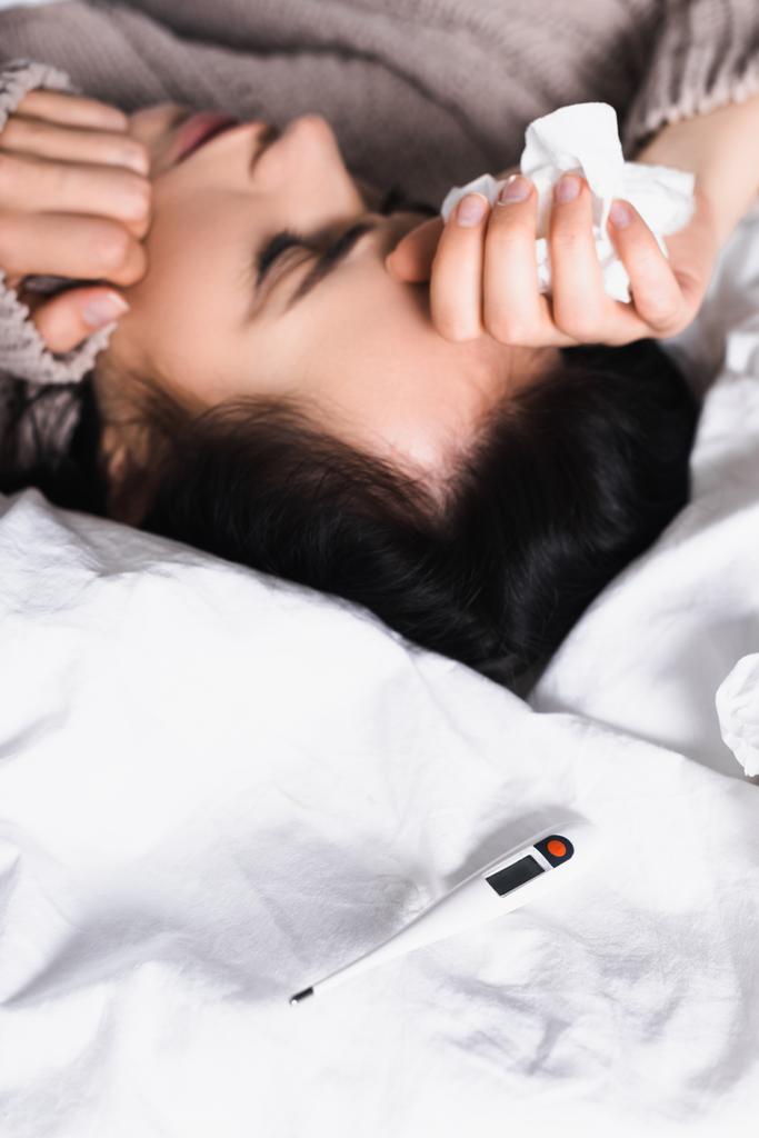 ziek jong brunette vrouw met thermometer en weefsel in bed - Foto, afbeelding