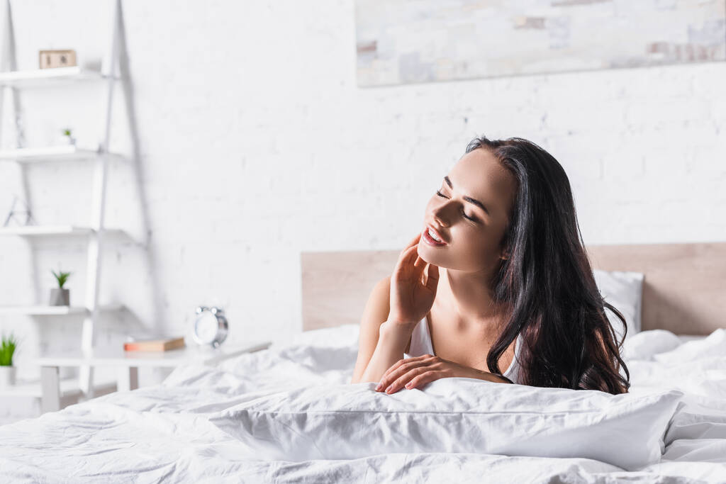 νεαρή μελαχρινή γυναίκα στο κρεβάτι με κλειστά μάτια - Φωτογραφία, εικόνα