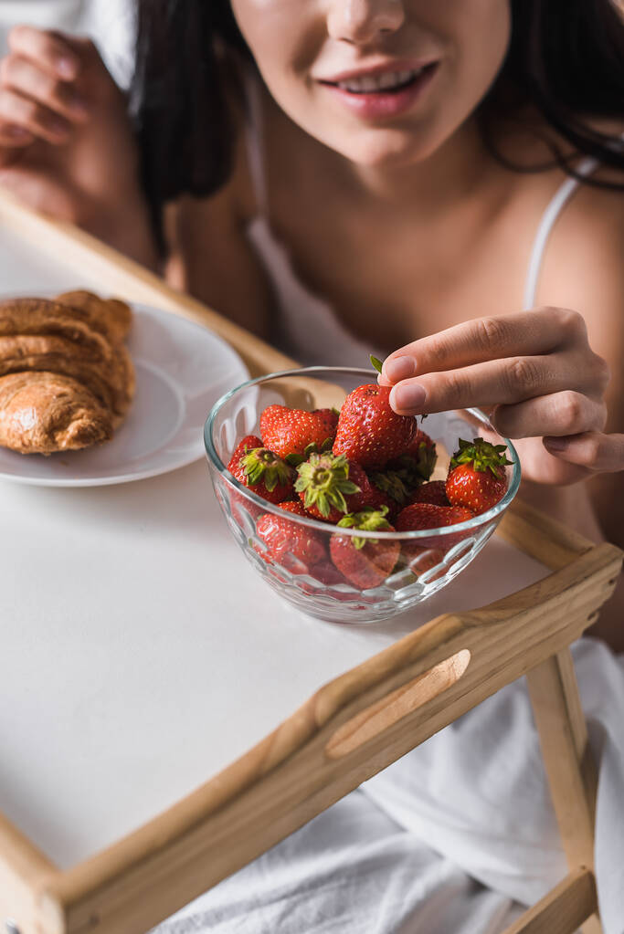 クロワッサンとイチゴをベッドで朝食に食べる女性の - 写真・画像