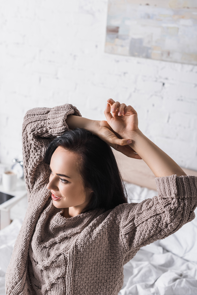 молодая брюнетка в свитере сидит в постели по утрам - Фото, изображение