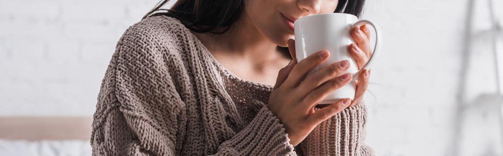 cropped view of young brunette woman in sweater with mug of hot cocoa at morning, banner - Photo, Image