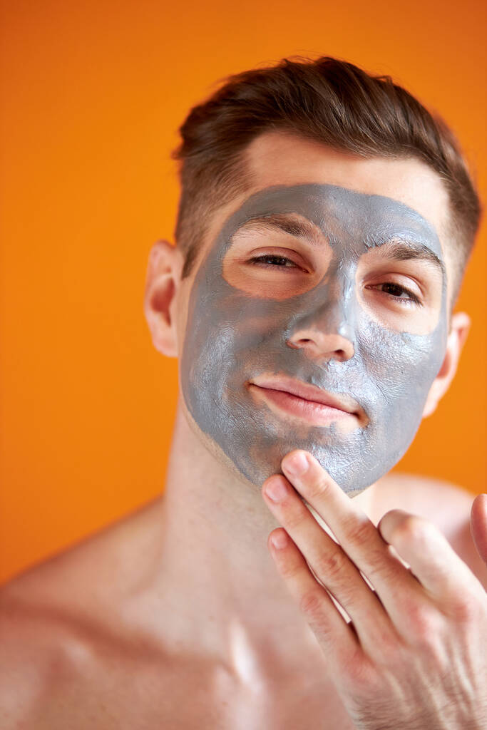 schöner junger Mann ohne Hemd mit kosmetischer Peelingmaske auf dem Gesicht - Foto, Bild