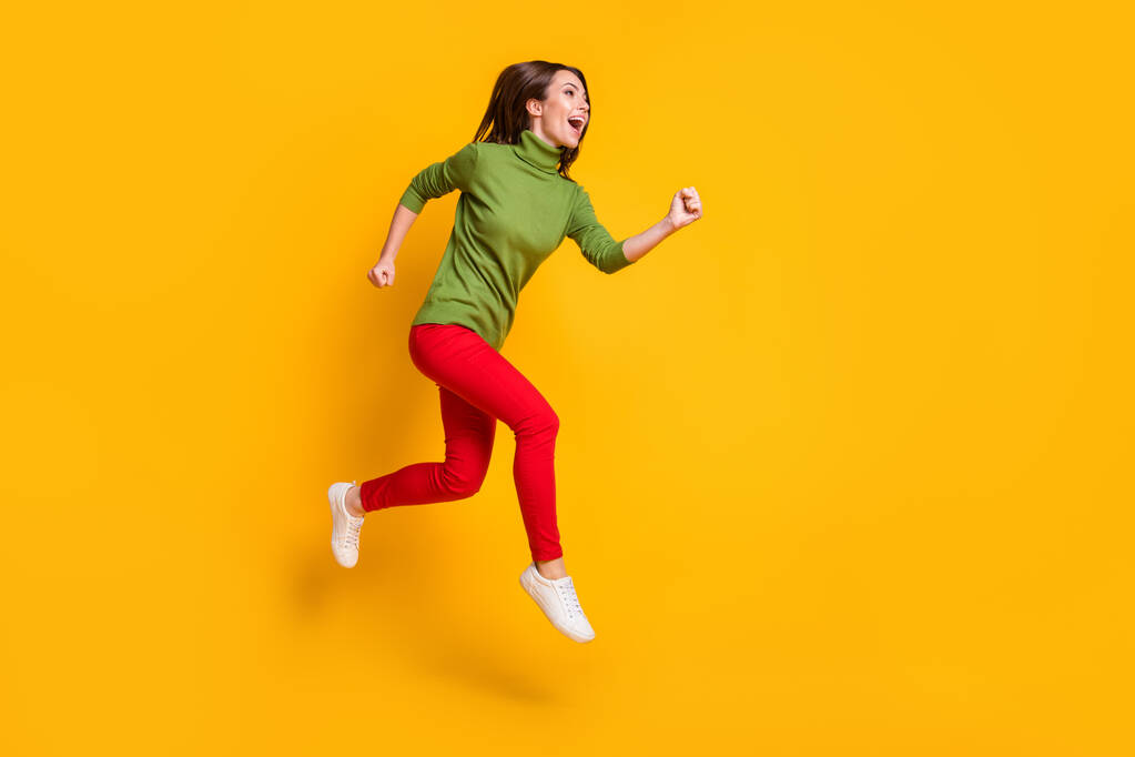 Dame springen aufgeregt stürzen tragen lässig grünen Pullover Schuhe rote Hose isoliert gelbe Farbe Hintergrund - Foto, Bild