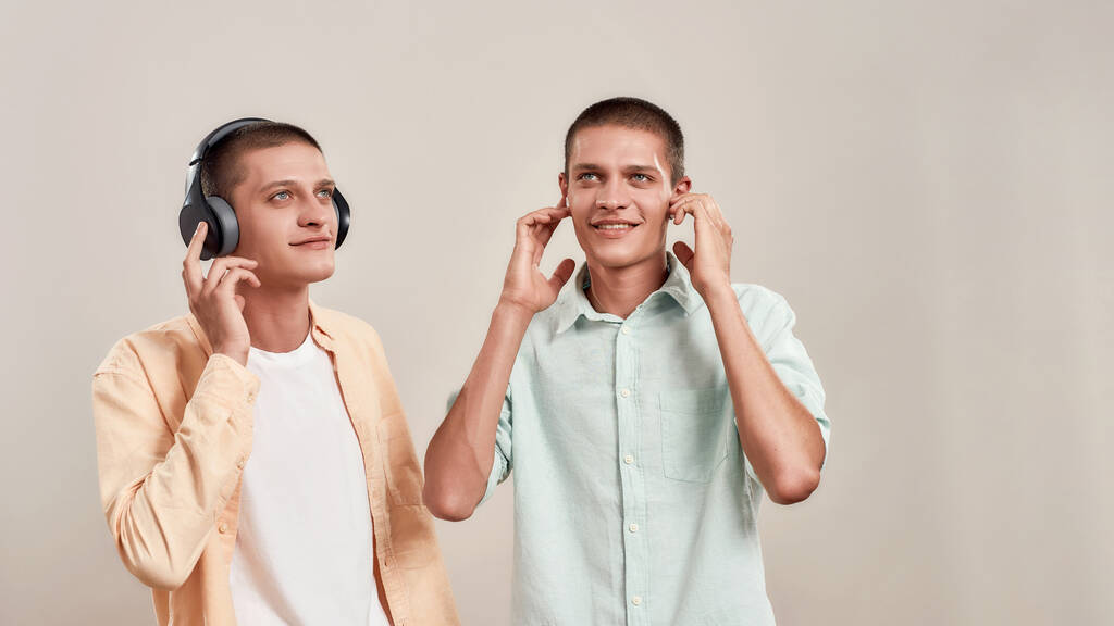 Mi piace la playlist preferita. Due giovani fratelli gemelli caucasici in abbigliamento casual ascoltare musica in cuffie e auricolari wireless - Foto, immagini