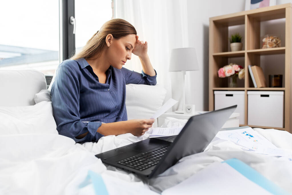 junge Frau mit Laptop und Papieren zu Hause im Bett - Foto, Bild