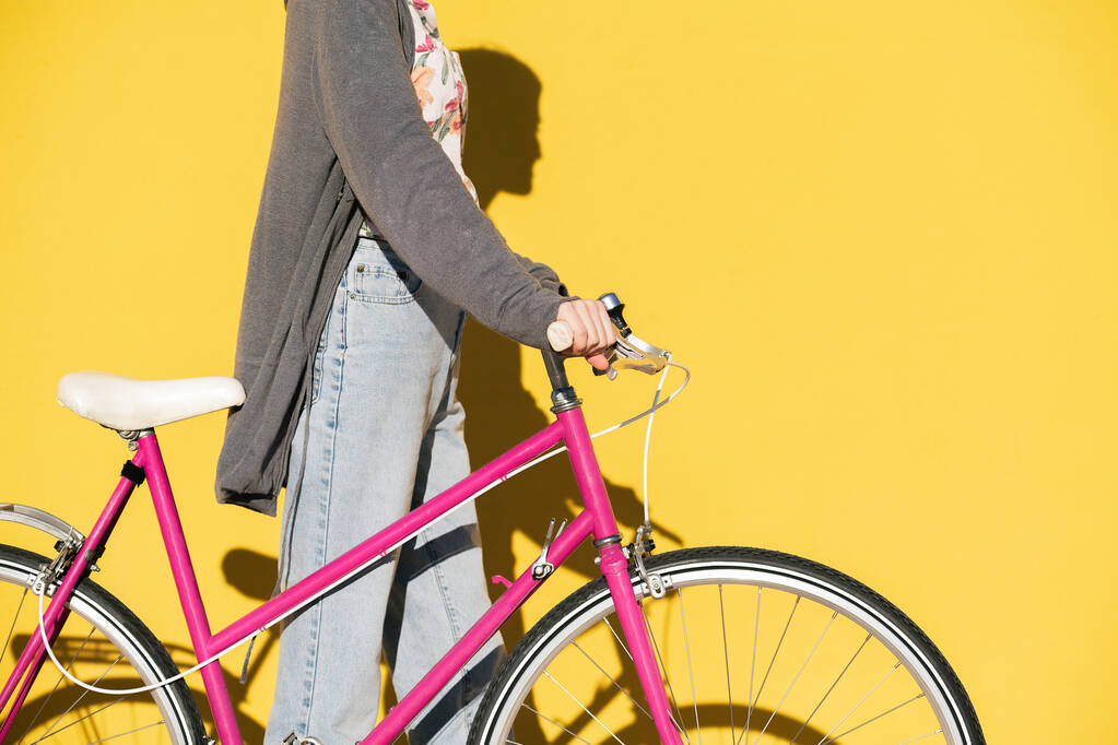 unrecognizable young woman walking with a pink retro bike in front of a colorful yellow wall, concept of active lifestyle and sustainable mobility, copy space for text - Foto, immagini