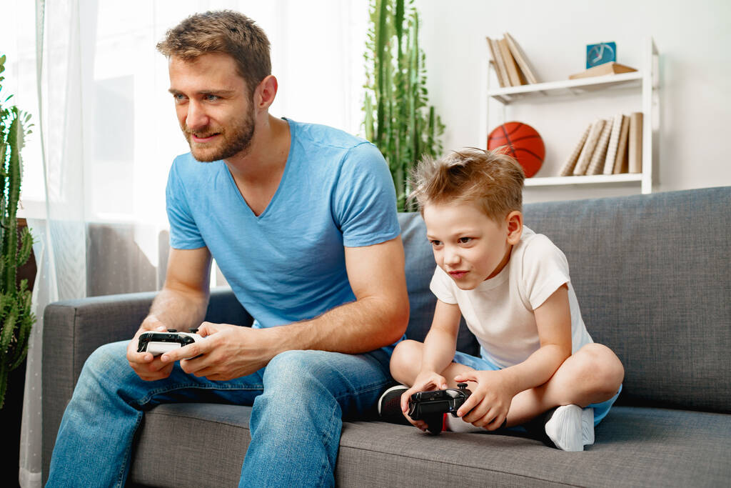 Ο πατέρας και ο γιος του παίζουν βιντεοπαιχνίδια μαζί στο σπίτι. - Φωτογραφία, εικόνα
