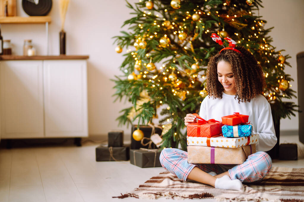 Boldog hölgy ajándékokkal a karácsonyfa mellett. Fiatal nő pózol ajándékokkal a karácsonyi belsőépítészetben. Divat, ünnep, ünnep koncepció. - Fotó, kép