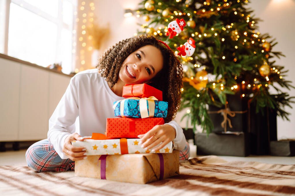 Onnellinen nainen, jolla on lahjoja joulukuusen lähellä. Nuori nainen poseeraa lahjoja joulun sisustus. Muoti, juhla, loma käsite. - Valokuva, kuva