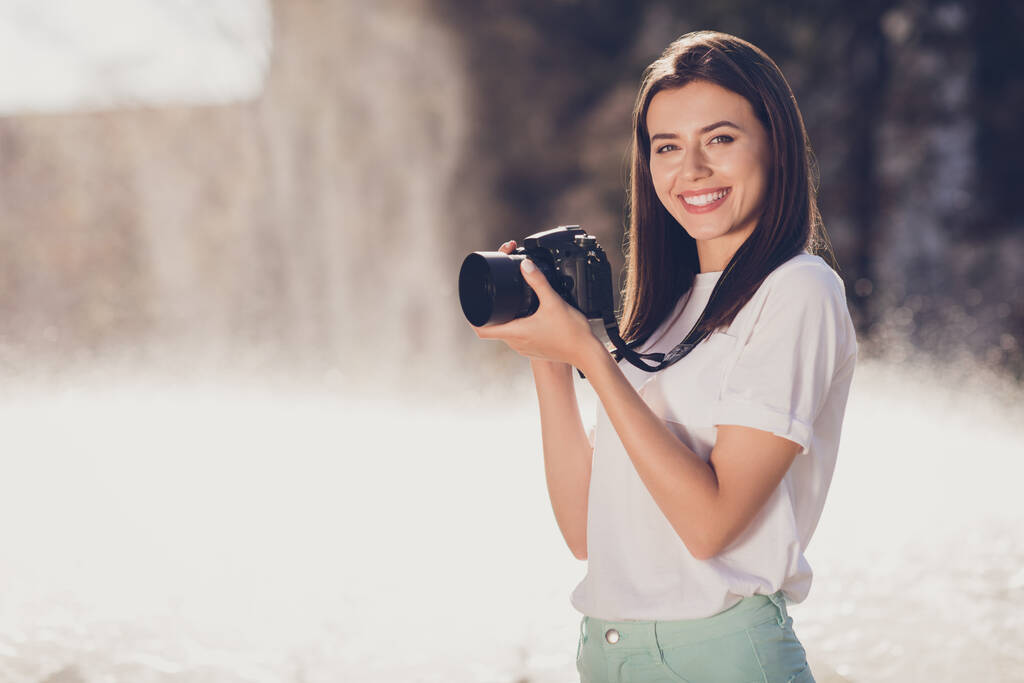 Φωτογραφία πορτρέτο της χαμογελαστή γυναίκα κρατώντας ψηφιακή φωτογραφική μηχανή με δύο χέρια σε εξωτερικούς χώρους - Φωτογραφία, εικόνα