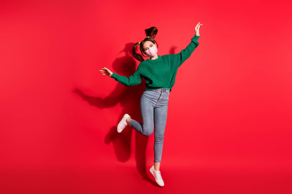 Фото привлекательной счастливой женщины прыгать воздух поднять руки носить маску защитные джинсы изолированы на красном фоне - Фото, изображение