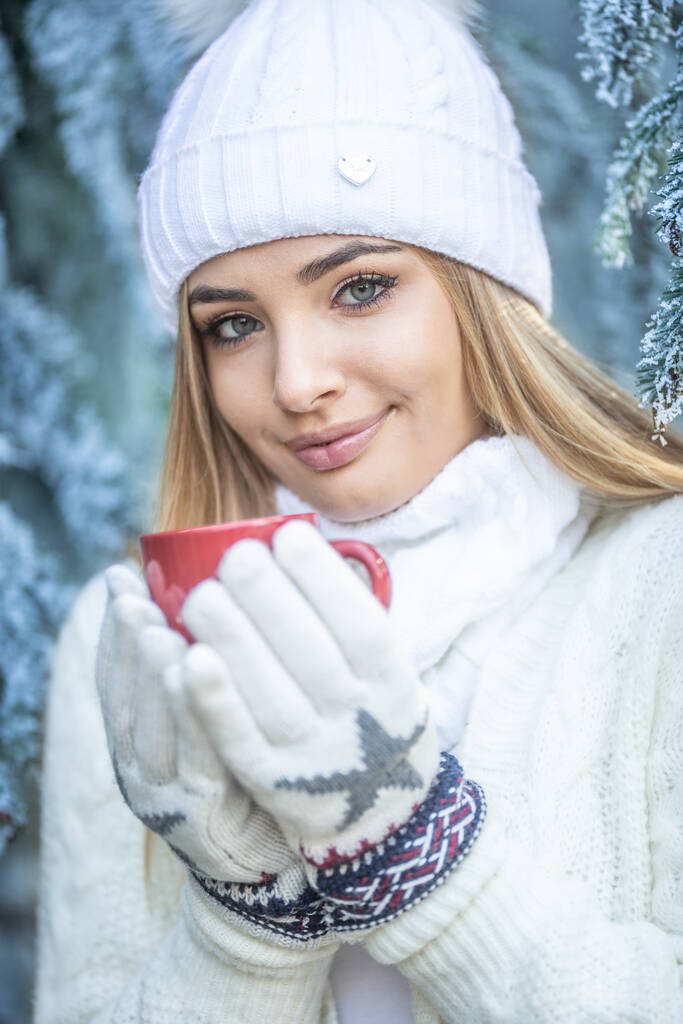 Blue eyes blonde girl holds hot drink in gloves on a freezing winter day outdoors. - Photo, Image