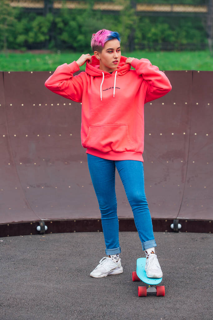 Ritratto di una bella ragazza alla moda in piedi accanto al campo da skateboard con il suo skateboard di plastica. - Foto, immagini