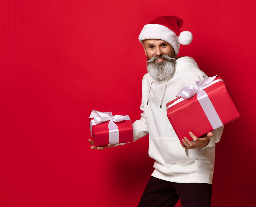 Man in a Santa hat with a surprised and embarrassed expression looks at the gifts. - Photo, Image