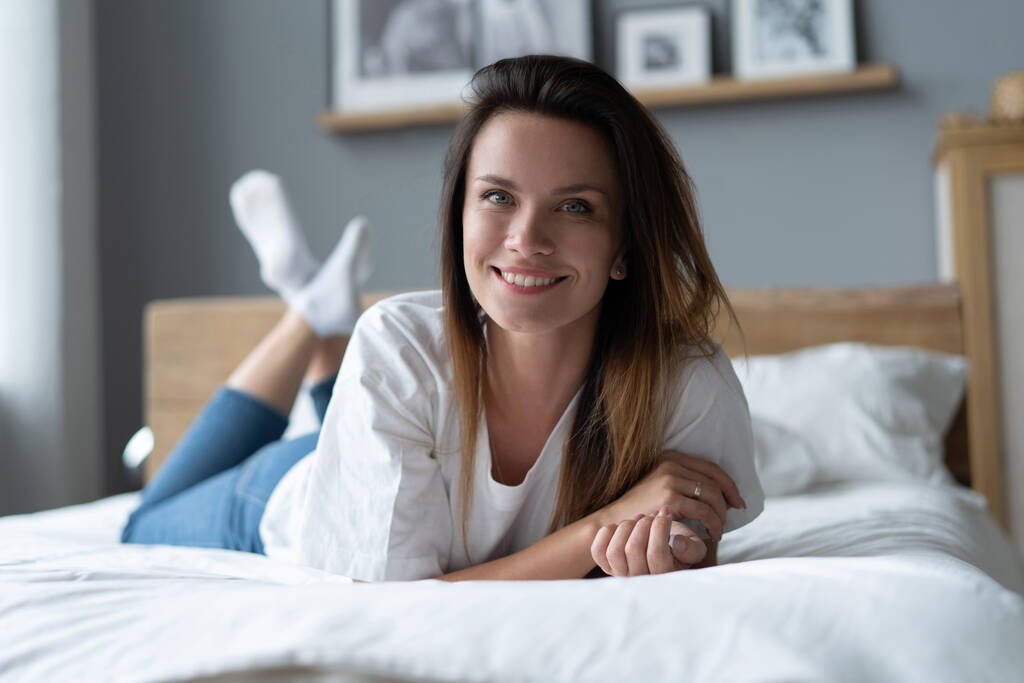 Πορτρέτο μιας χαμογελαστής όμορφης νεαρής γυναίκας ξαπλωμένης στο κρεβάτι. - Φωτογραφία, εικόνα