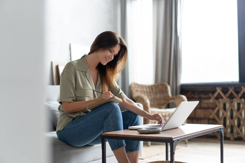 Kobieta używająca laptopa w salonie. Pracuje w domu w zamknięciu kwarantanny. Odległość społeczna. - Zdjęcie, obraz